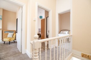 Una escalera con barandilla blanca que lleva a un dormitorio con cama y mesita de noche.