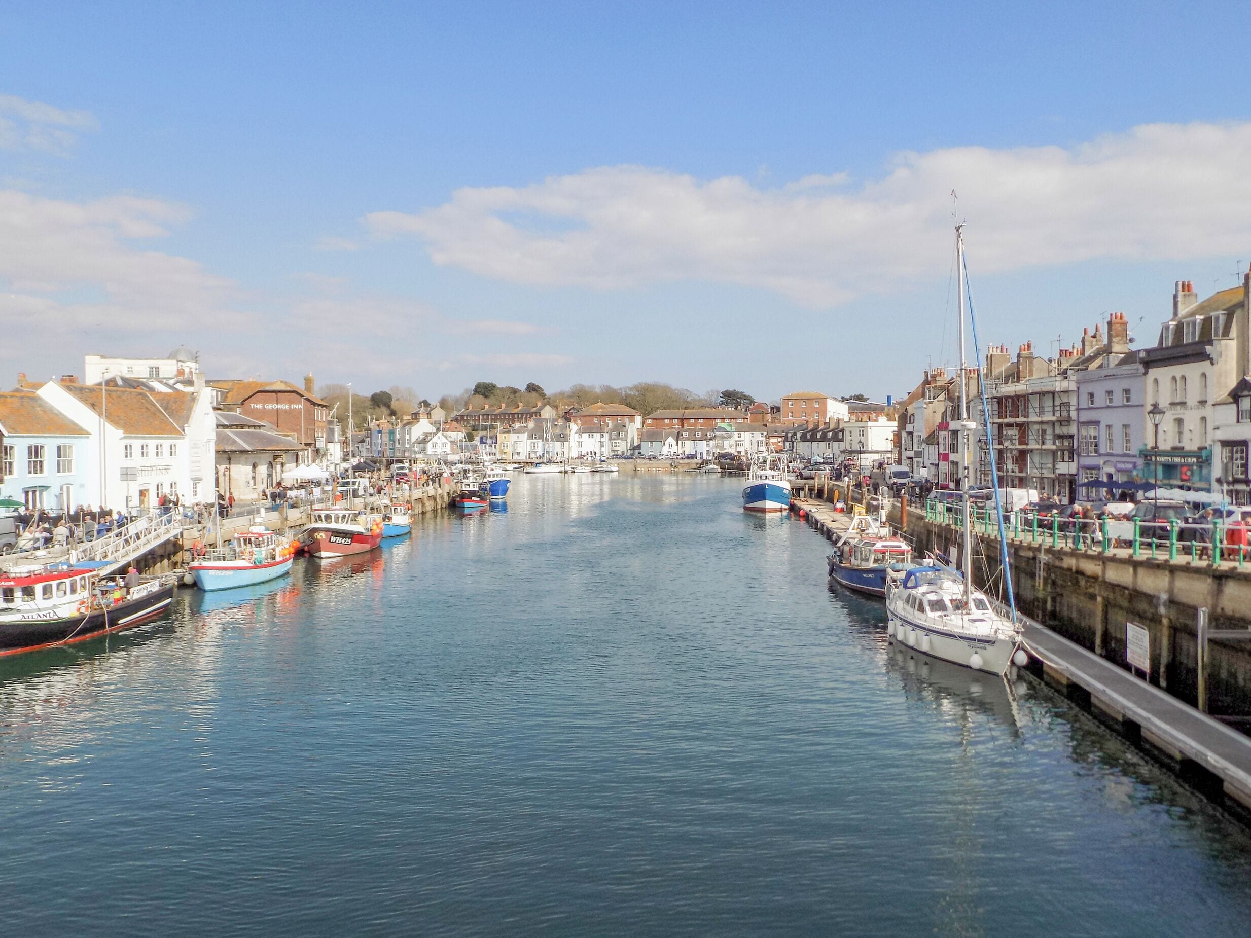 A harbor with boats docked along the waterfront, surrounded by buildings and a clear sky.