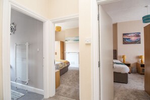 Un pasillo que conduce a un dormitorio con cama, mesitas de noche y un cuadro en la pared.