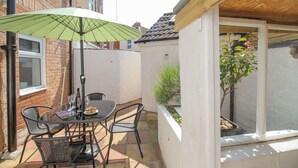 A patio with a table and chairs, a green umbrella, and a small garden area. - The Skipper's House (Weymouth)