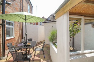 Un patio con mesa y sillas, una sombrilla verde y un pequeño jardín.