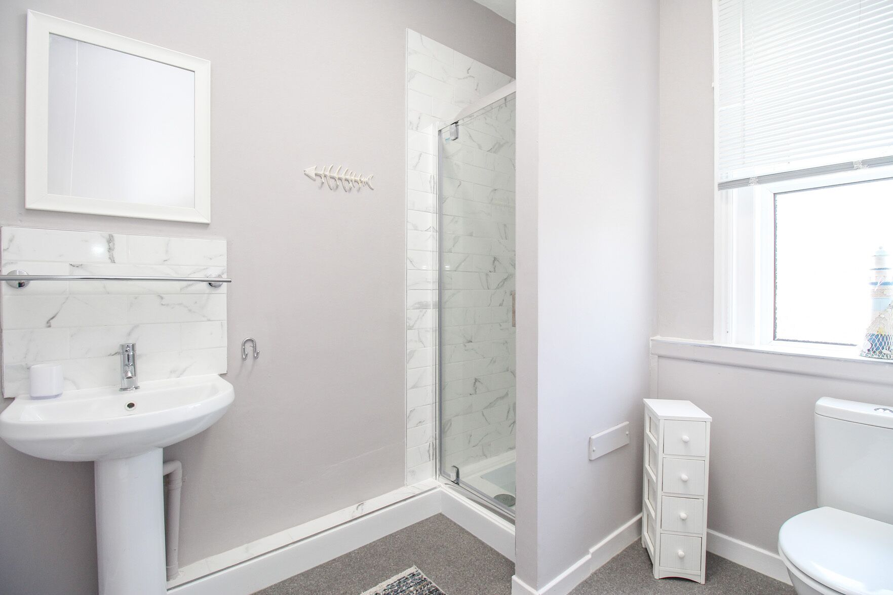 Une salle de bain moderne avec un lavabo blanc, un miroir et des toilettes. Elle est dotée d’une douche à parois de verre et d’un espace de douche carrelé en marbre.