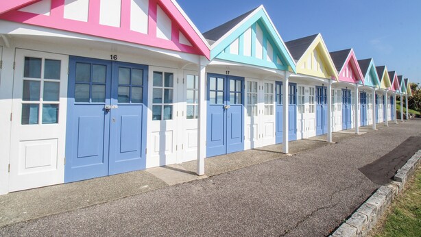 A row of colorful beach huts numbered 16 to 17, with a gravel path in front. - The Skipper's House (Weymouth)