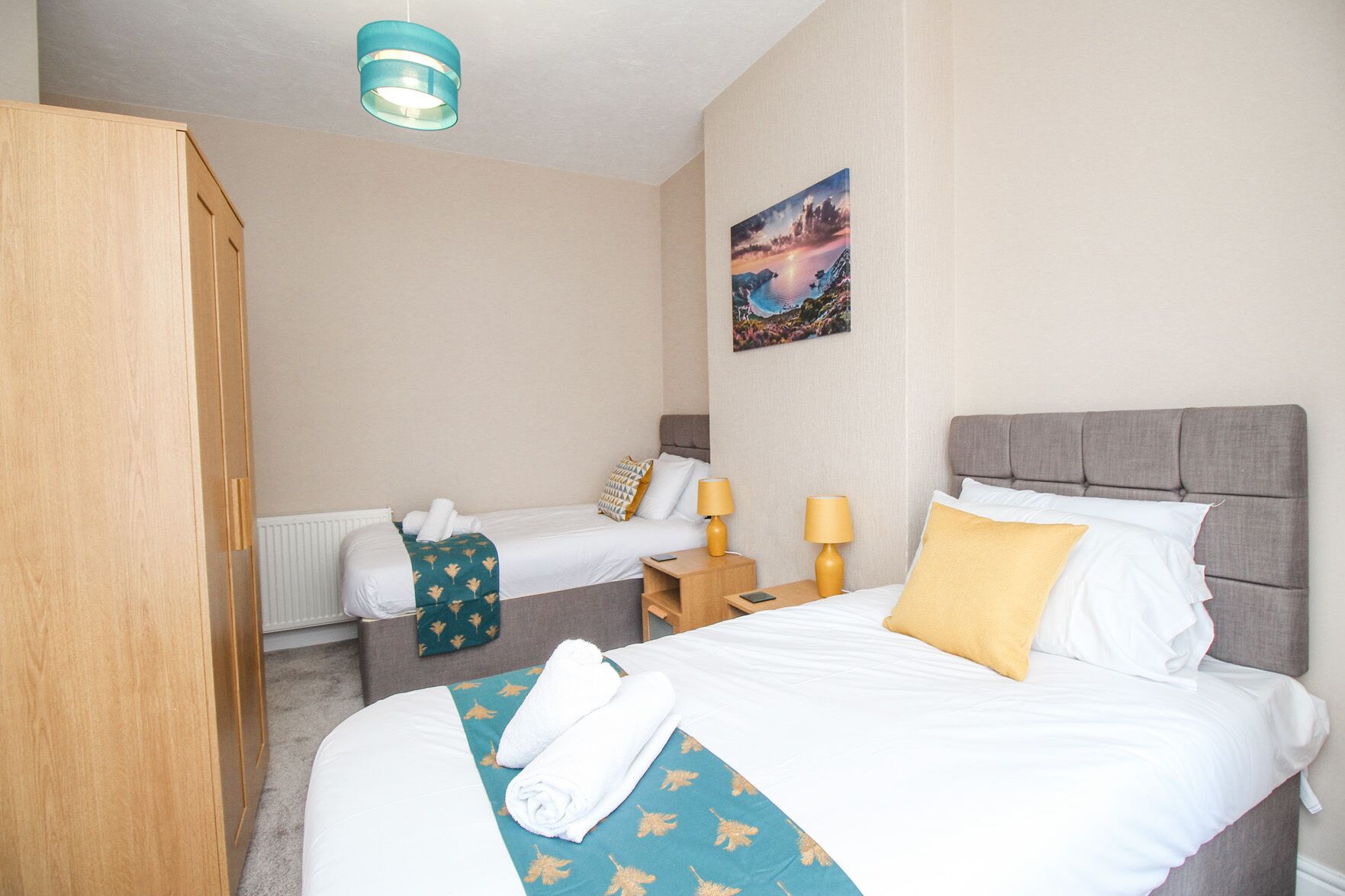 A hotel room with two beds, a wardrobe, a painting on the wall, and a ceiling light.