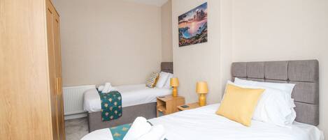 A hotel room with two beds, a wardrobe, a painting on the wall, and a ceiling light.