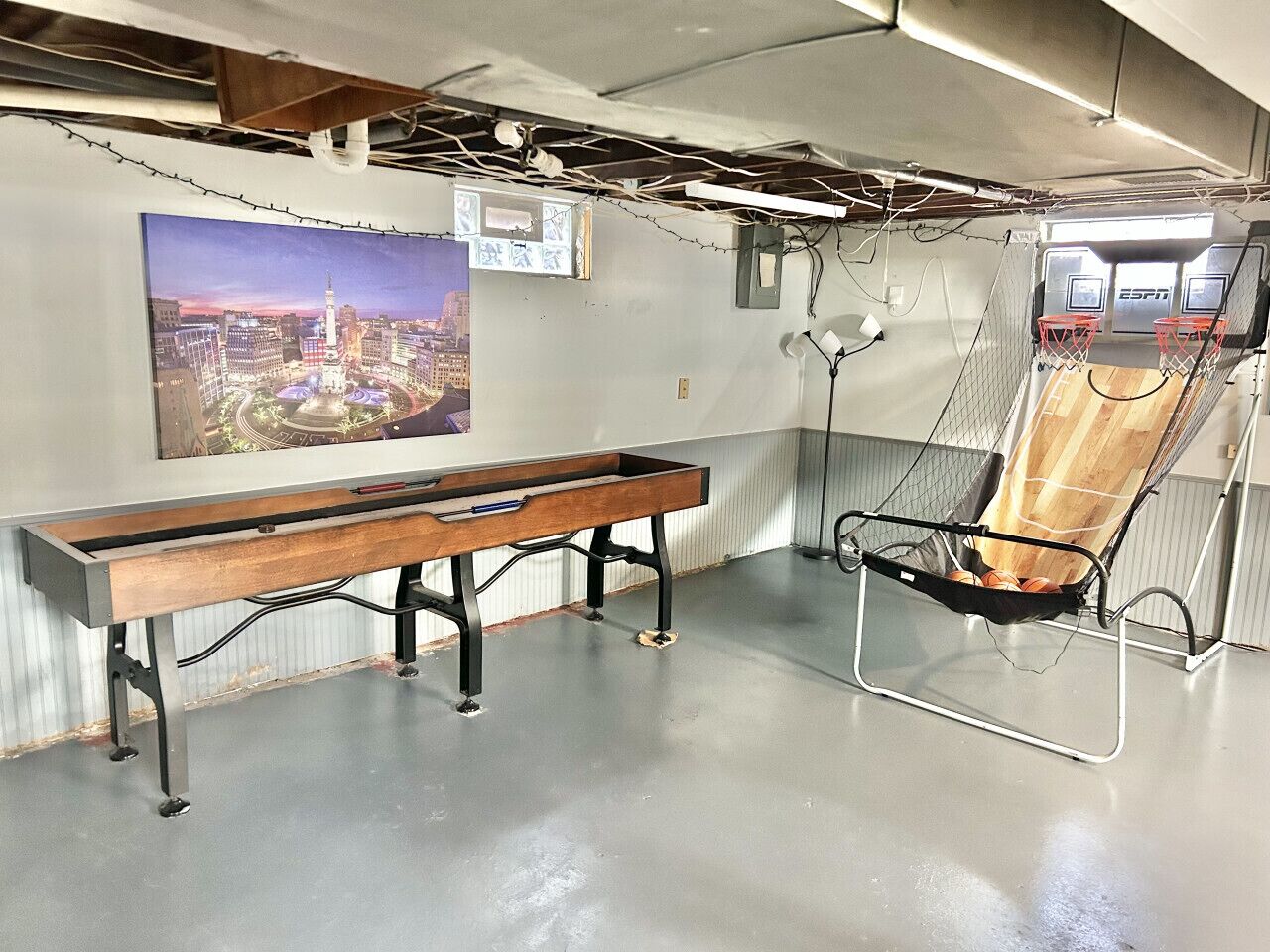 A room with a long wooden bench, a hanging chair, a basketball hoop, and a cityscape poster on the wall.