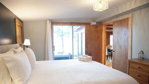A neatly made bed with white linens, a bedside lamp, and a wooden wardrobe. - Lakefront Cottage: Dock & Fire Pit- Pet Friendly (Geneva)