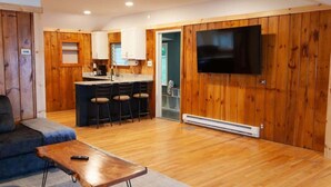 A modern living room with a wooden floor, a sofa, a coffee table, and a TV mounted on the wall. - Lakefront Cottage: Dock & Fire Pit- Pet Friendly (Geneva)