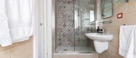 Casa de banho moderna com chuveiro, lavatório e painel de azulejos estampado.