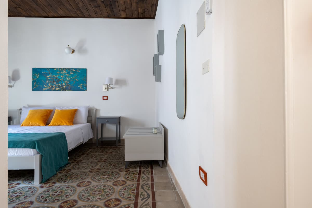 Een slaapkamer met een bed, nachtkastje, spiegel en een kunstwerk aan de muur.