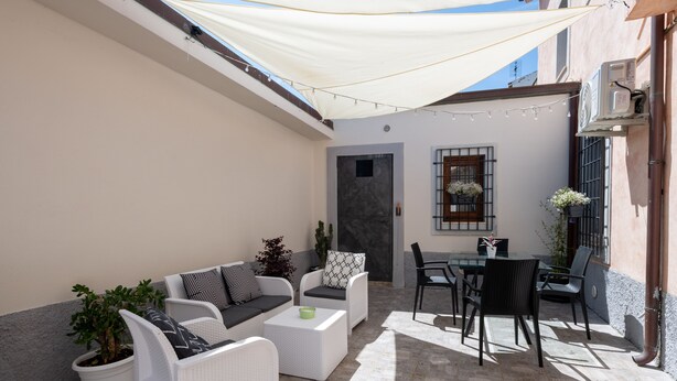 A sunlit patio with white wicker furniture, a dining table, and potted plants. - Don Pedro 53 (Tresnuraghes)