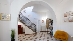 A spacious foyer with a checkered floor, a staircase with a wrought iron railing, and a yellow armchair. - Don Pedro 53 (Tresnuraghes)
