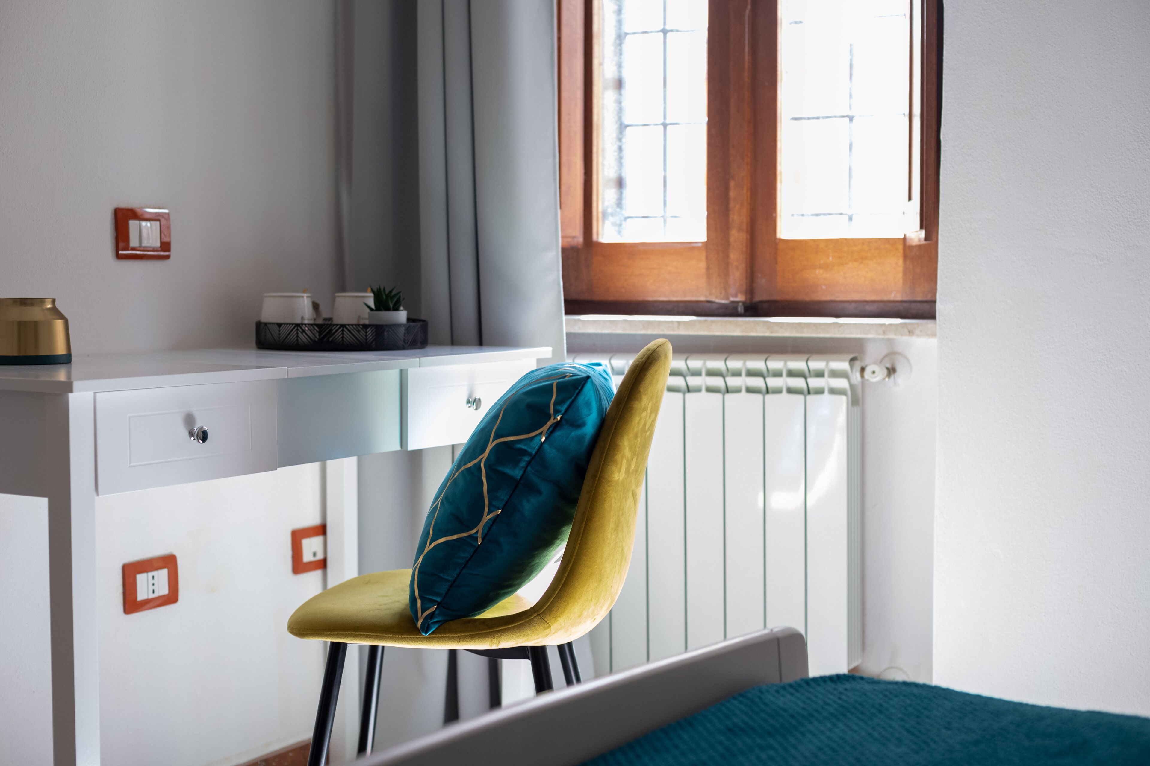 Een kamer met een bed, een bureau met stoel, een radiator en een raam met gordijnen.