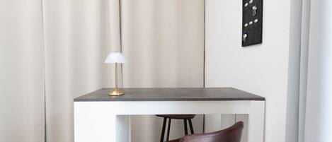 A small, modern room with a white table, a brown chair, a lamp, and a wall-mounted light switch.