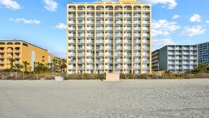 A high-rise hotel with multiple balconies, a sandy beach in the foreground, and a clear sky. - Oceanfront Efficiency T508 (Myrtle Beach)