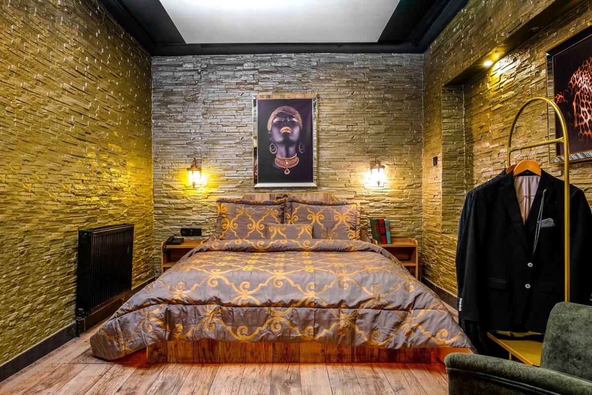 A bedroom with a large bed, a wooden floor, a brick wall, and a framed artwork above the bed.
