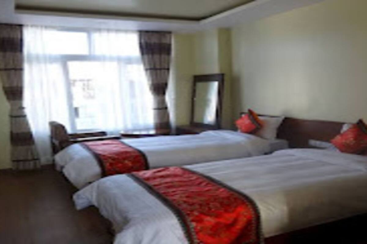 Habitación de hotel con dos camas, un ventanal con cortinas, un espejo y cabecero de madera.