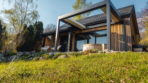 Una casa moderna con un'ampia vetrata, un patio in legno e un vialetto in pietra.