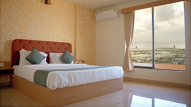 A bedroom with a large bed, a ceiling fan, an air conditioning unit, and a view of the sea through a large window. - The Sky Comfort Beach Hotel, Dwarka (Dwarka)