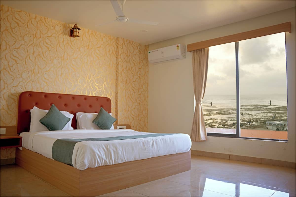 Une chambre dotée d’un grand lit, d’un ventilateur de plafond, d’un appareil de climatisation et offrant une vue sur la mer grâce à une grande fenêtre.