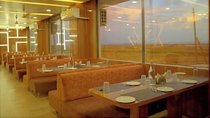 A restaurant with booths and tables, large windows with a view of the countryside, and modern lighting fixtures. - The Sky Comfort Beach Hotel, Dwarka (Dwarka)