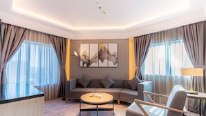 A modern hotel room with a sofa, armchair, coffee table, and artwork on the wall.