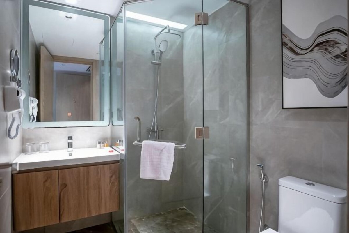 Un baño con ducha envuelta en vidrio, lavamanos con espejo y retrete.
