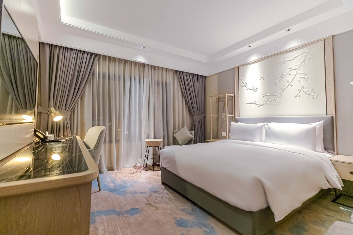Ein modernes Hotelzimmer mit einem großen Bett, einem Schreibtisch mit Stuhl, einem kleinen Beistelltisch und einem großen Spiegel.