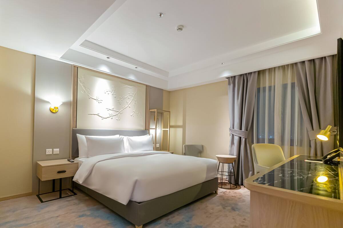 Ein Hotelzimmer mit einem großen Bett, Nachttisch, Lampe, Stuhl und einem Schreibtisch mit Lampe.