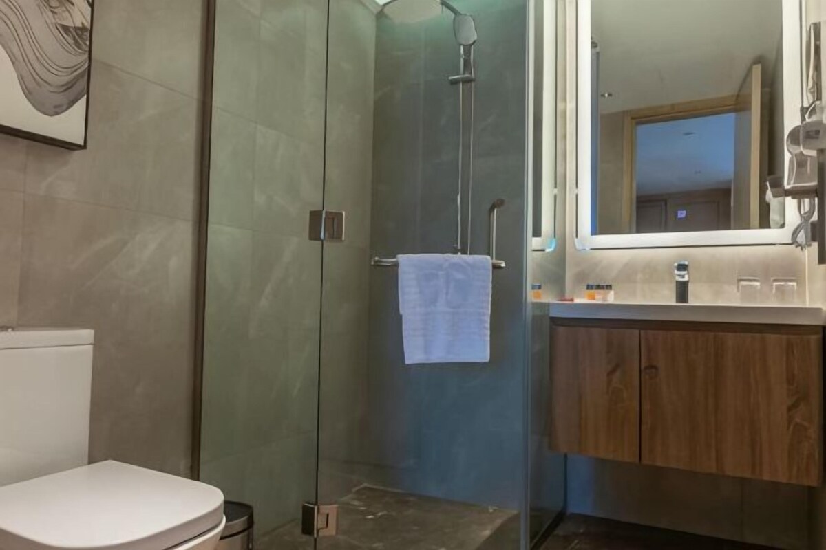Un baño con ducha envuelta en vidrio, un inodoro blanco y un tocador de madera con espejo.