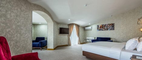 A hotel room with a bed, a red chair, a blue chair, a TV, and a painting on the wall.