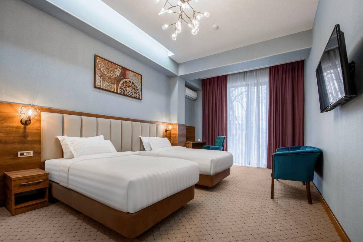A hotel room with a large bed, a smaller bed, a TV, a chair, and a decorative wall piece.
