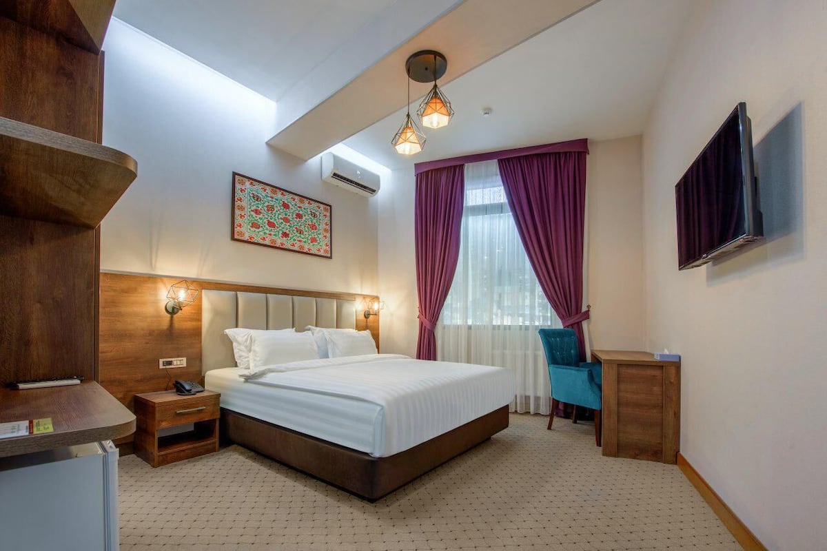 A hotel room with a large bed, a desk, a chair, a TV, and a decorative wall piece.