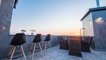 Una terraza en la azotea con mobiliario exterior, vistas al atardecer y una chimenea.