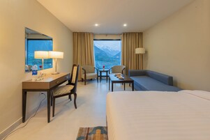 Habitación de hotel con cama, escritorio, silla y sofá. Se ve una ventana con vistas a las montañas.