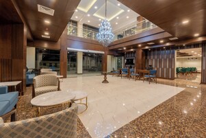 Un vestíbulo espacioso con un alto techo, una araña y una zona de estar con mesas y sillas.