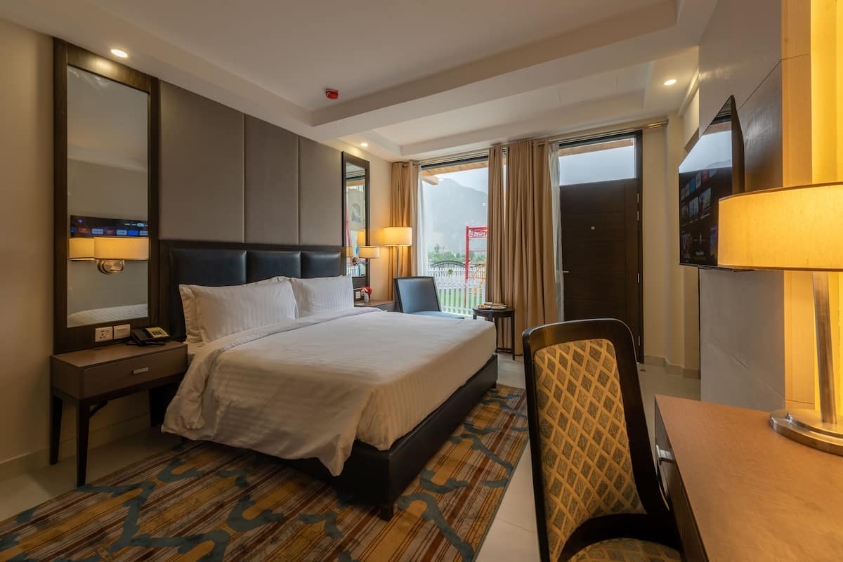 A hotel room with a large bed, bedside tables, a desk, a chair, a TV, and a view of the outdoors.