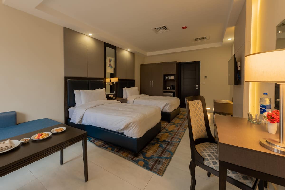 A hotel room with two beds, a sofa, a dining table, and a TV.