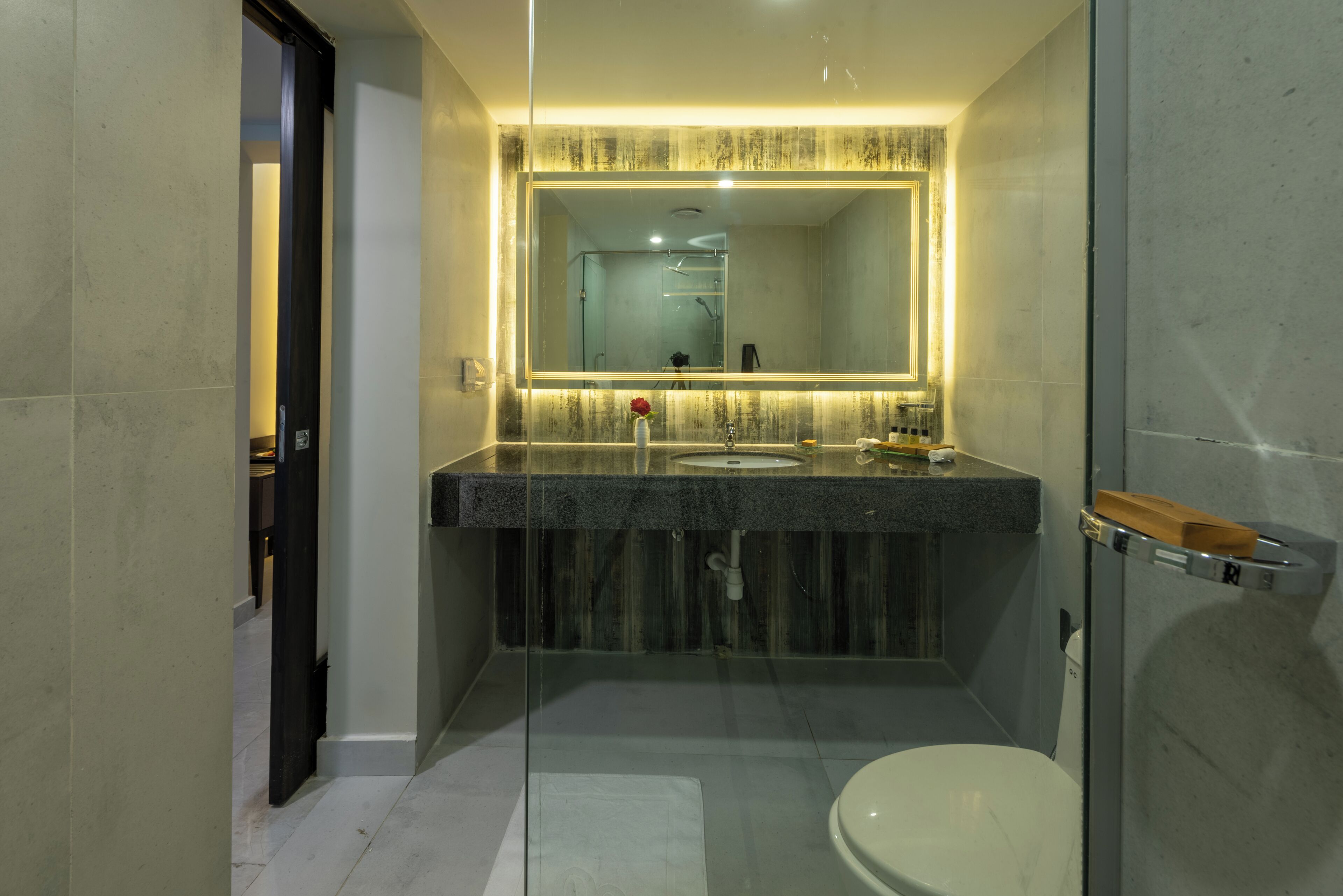 A modern bathroom with a glass shower enclosure, a large mirror, and a marble countertop.