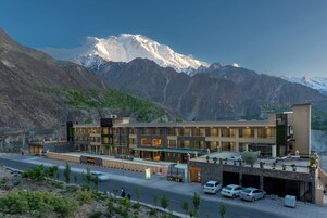 Un hotel moderno con un paisaje montañoso, que presenta una estructura de varios pisos, un estacionamiento y vistas de picos nevados.