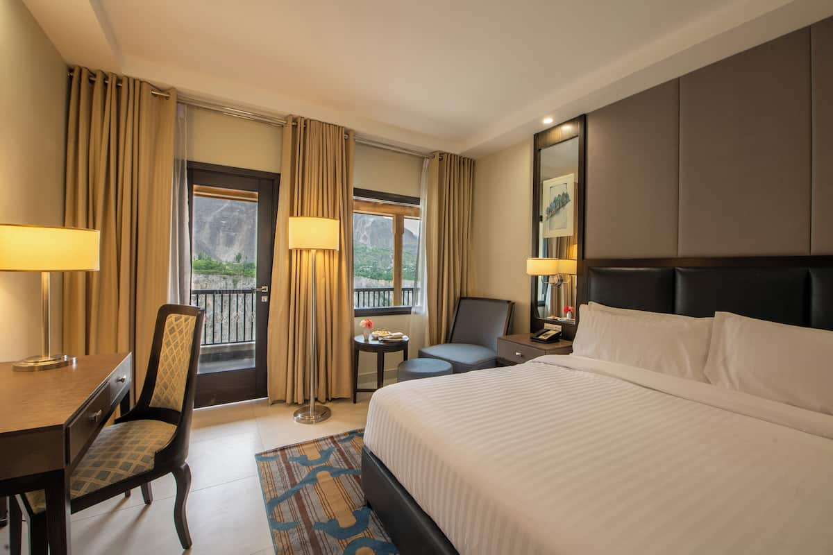 A hotel room with a bed, desk, chair, and a view of the outdoors.