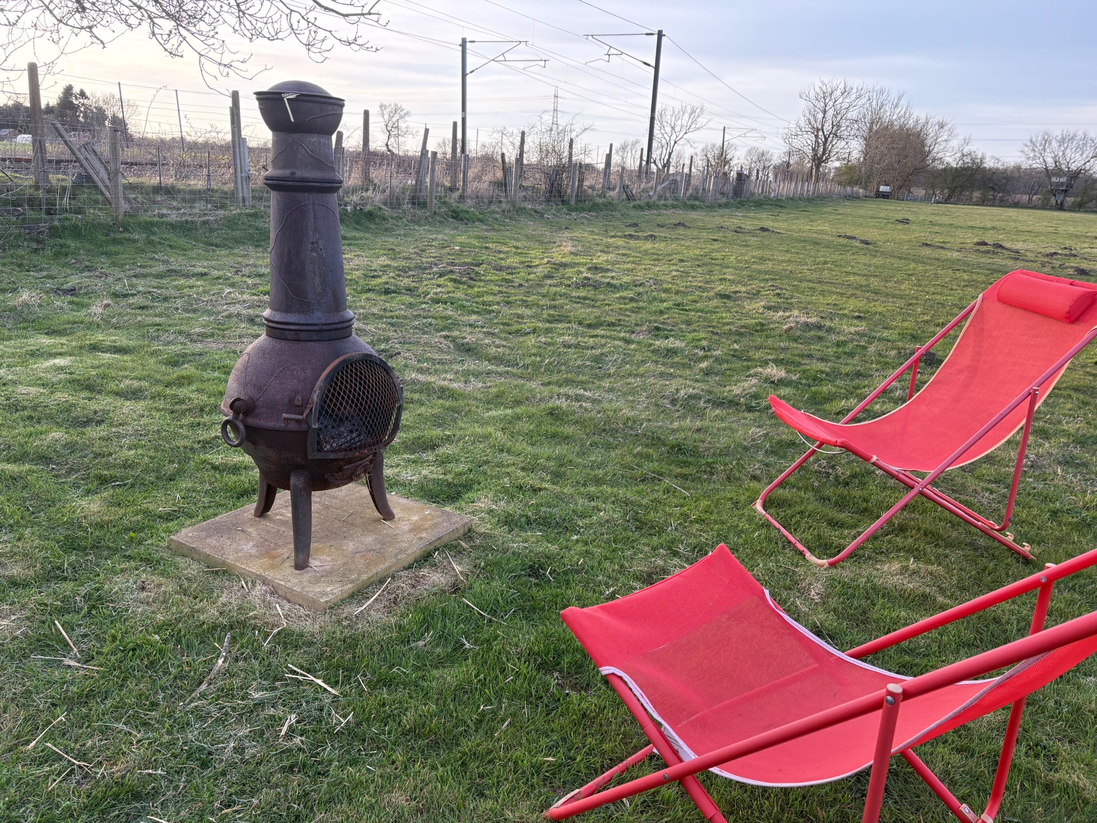 A rustic outdoor area with a metal stove on a concrete base and two red folding chairs.