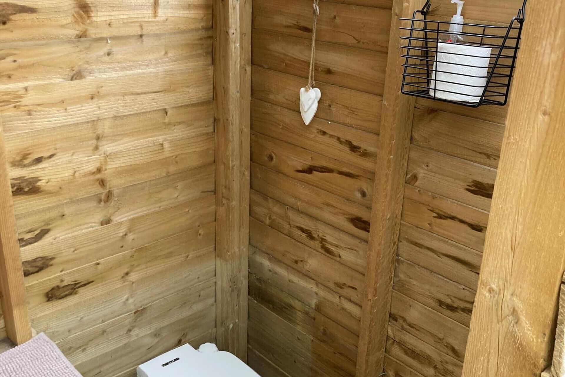L’intérieur d’un chalet en bois, avec un mur en bois, une décoration en forme de cœur suspendue et une étagère en métal noir sur laquelle se trouvent une boîte de mouchoirs et une bouteille.