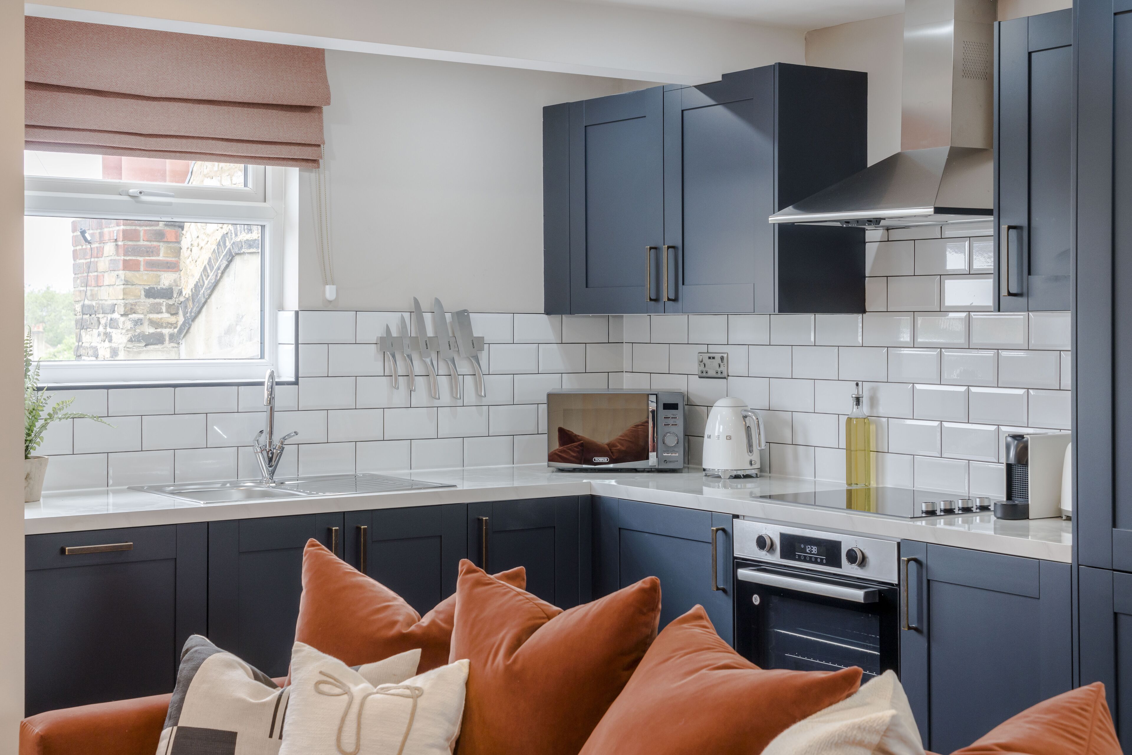 A modern kitchen with dark blue cabinets, white countertops, and a built-in oven.