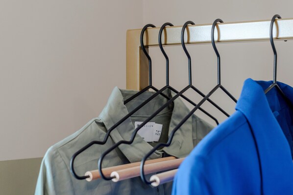 A clothing rack with various garments, including a blue jacket and a green shirt. - Your Apartment Shepherd's Bush (London)