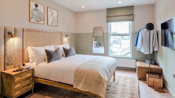 Un dormitorio moderno con una cama grande, mesitas de noche, un espejo y una ventana con vistas.