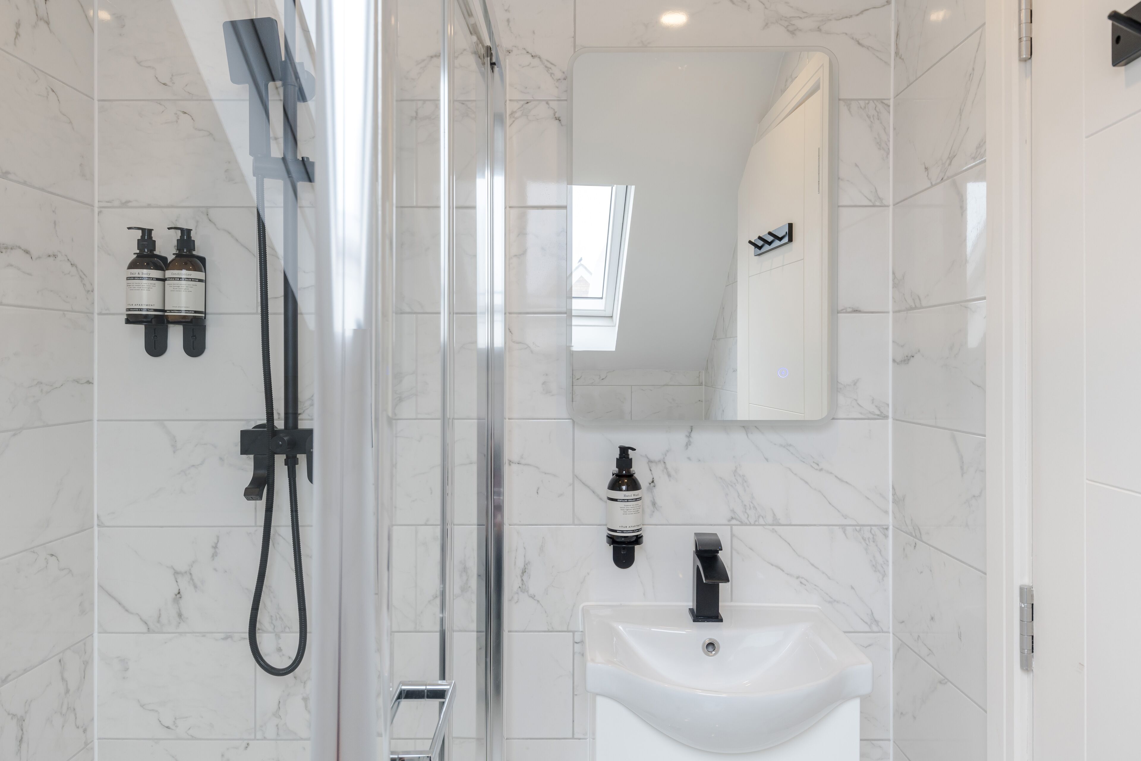 A modern bathroom with a glass-enclosed shower, a white sink, and two bottles of shampoo on the wall.