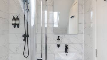 A modern bathroom with a glass-enclosed shower, a white sink, and two bottles of shampoo on the wall.