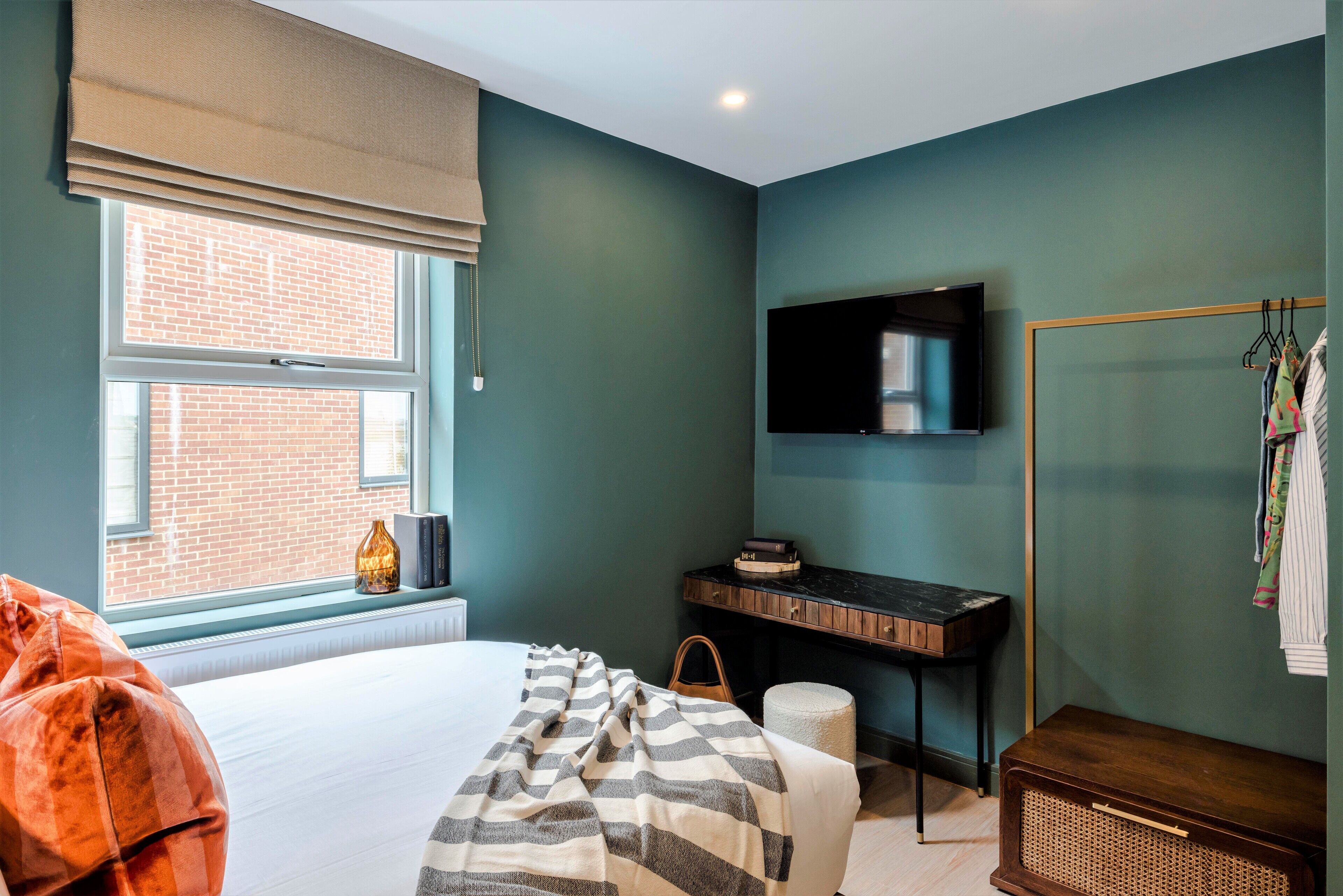 A bedroom with a bed, a desk, a television, and a window with a view of a brick building.