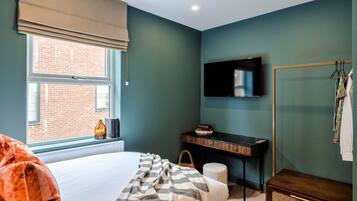 A bedroom with a bed, a desk, a television, and a window with a view of a brick building.